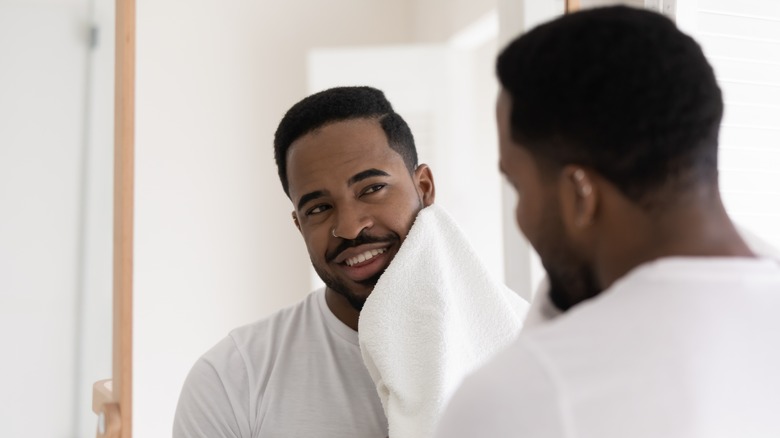Man wiping face with towel and looking in mirror