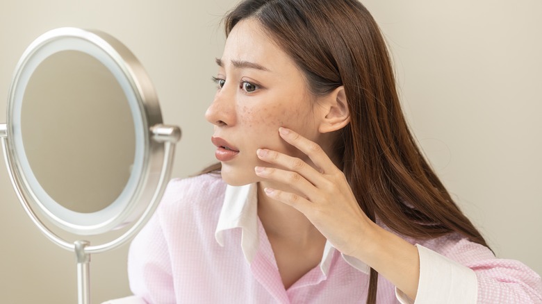 Woman examines acne in mirror 