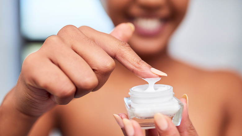 A woman smiling at her jar of skincare cream