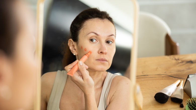 A woman applying liquid blush on her cheek while looking in the mirror