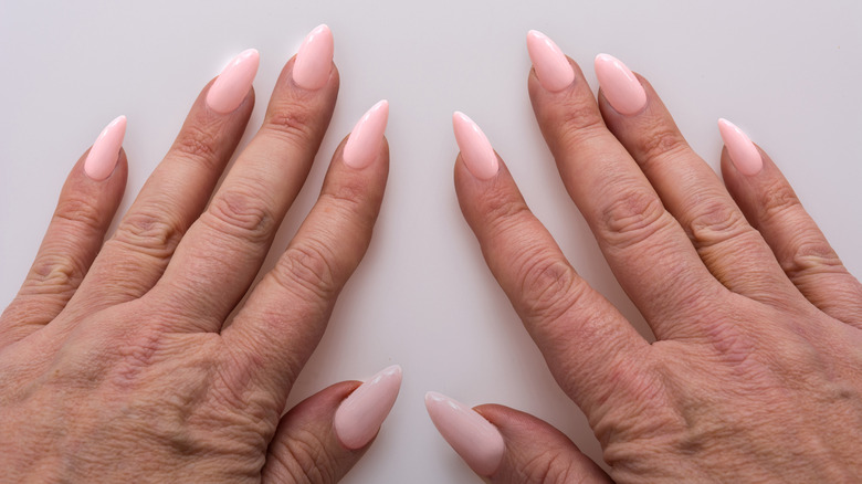 Middle-aged hands with light-pink stiletto nails.