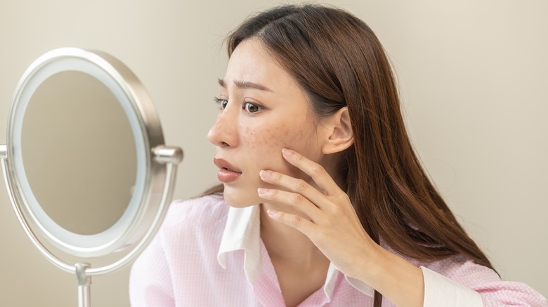 Woman looking at skin on her face in a mirror