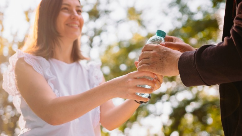 Woman handing homeless man water