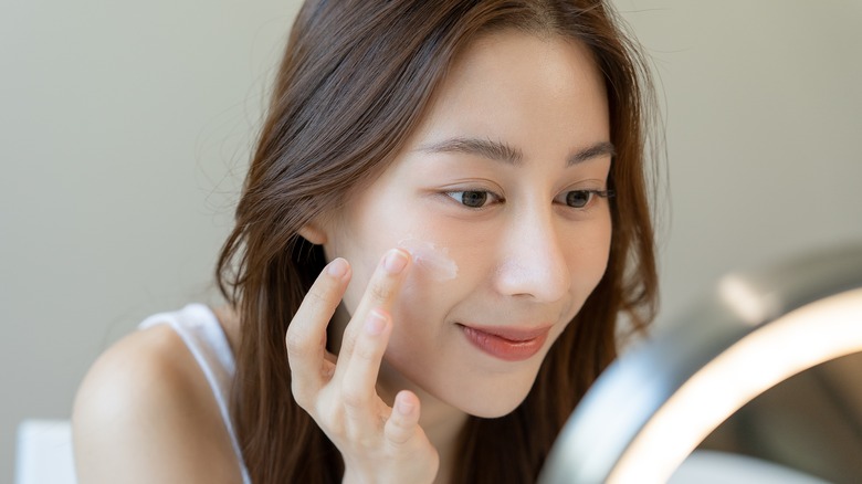 smiling woman applying face moisturizer 