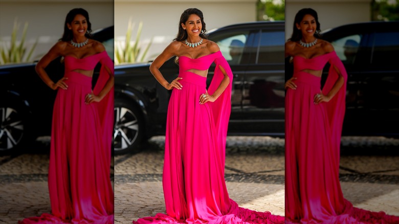 A woman wearing a hot pink dress with a flowing sleeve and cutout.