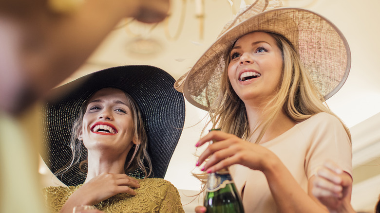 Two women wearing large hats at an elegant party.