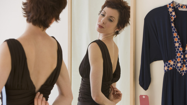 A woman trying on a formal black dress.