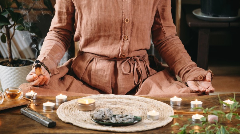 Woman meditates with candles and sage