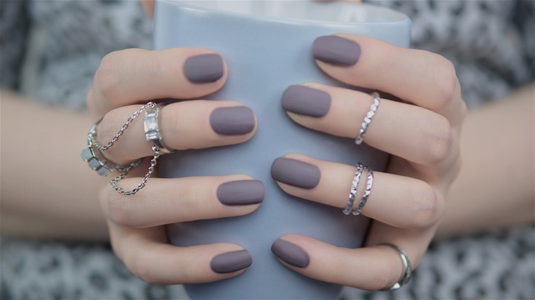 Person holding mug with mauve nails and finger jewelry