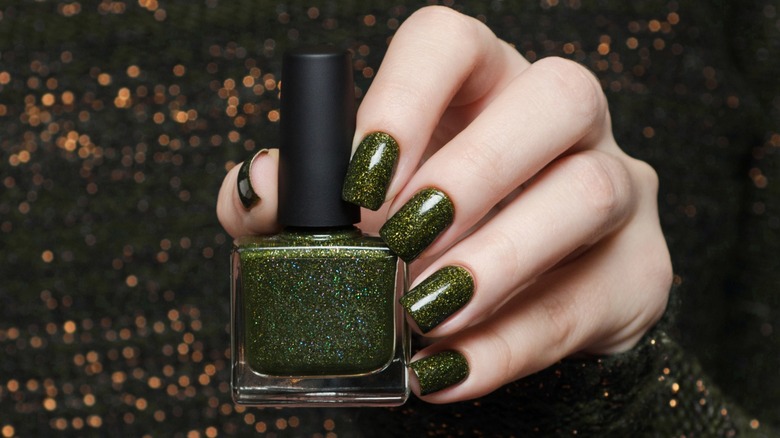 Person with green sparkling nails holding polish bottle