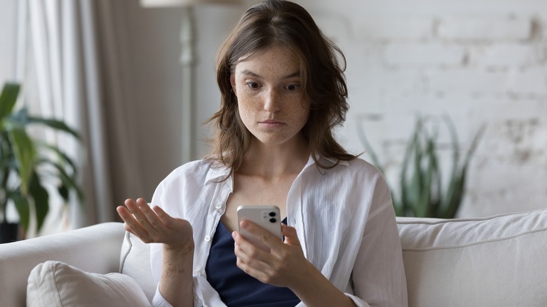 Woman looks at smart phone while appearing confused 