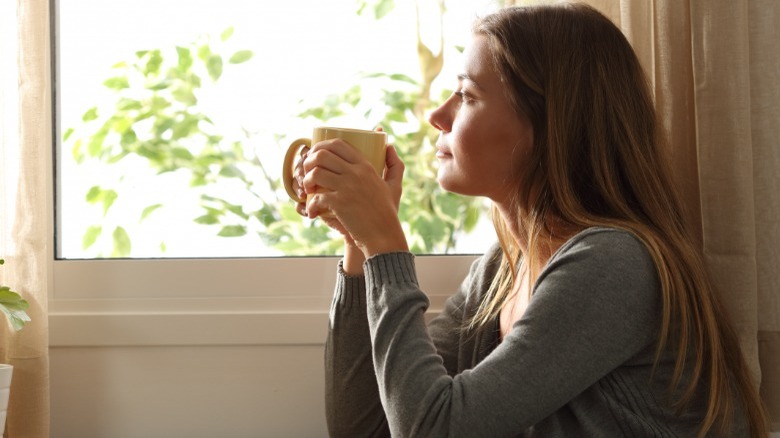 Woman holding coffee looking outside