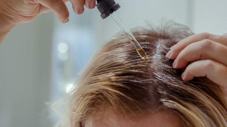 Close up of hair model applying oil to scalp