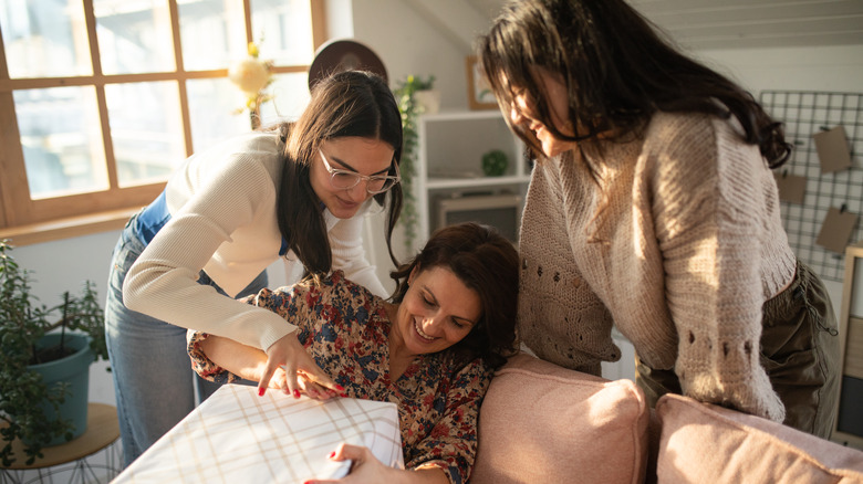 Daughters helping mother open gift