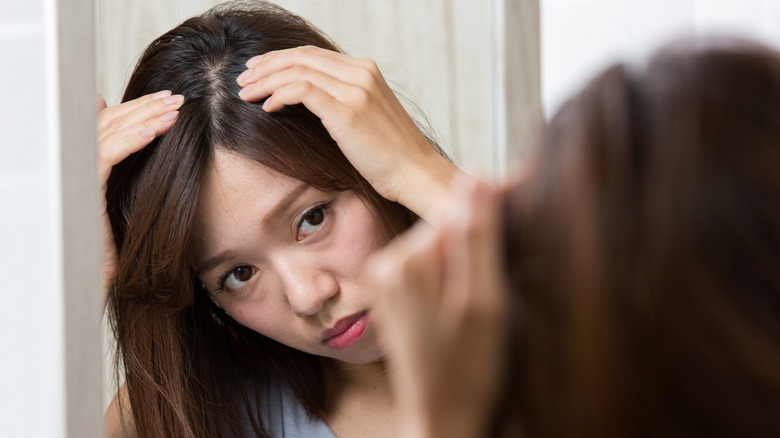 Woman examines scalp in mirror