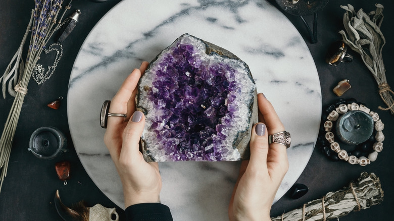 hands holding amethyst on marble and black background