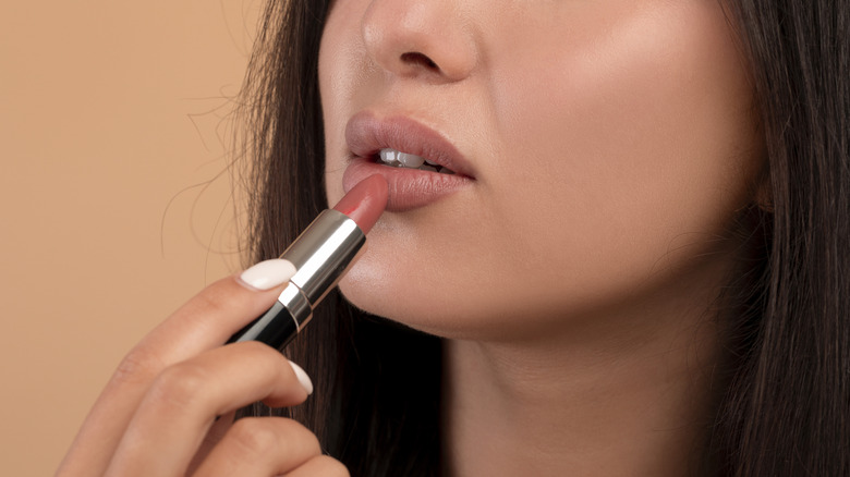 A woman applying red lipstick to her lips.