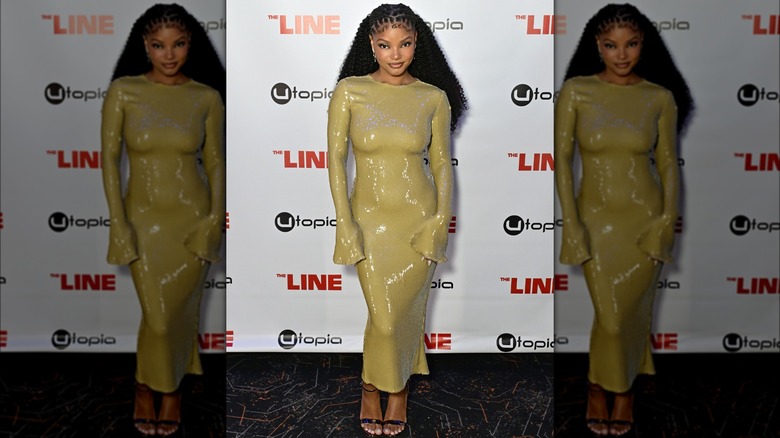 Halle Bailey posing on a red carpet in a mustard yellow glitter dress.