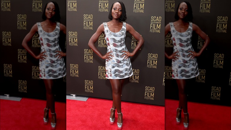 Lupita Nyongo posing on a red carpet in a silver minidress.