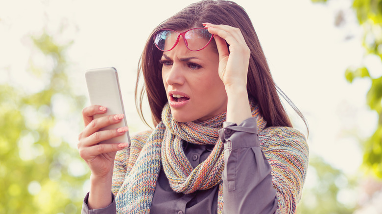 Woman looks exasperated at ingredient list on cell phone 