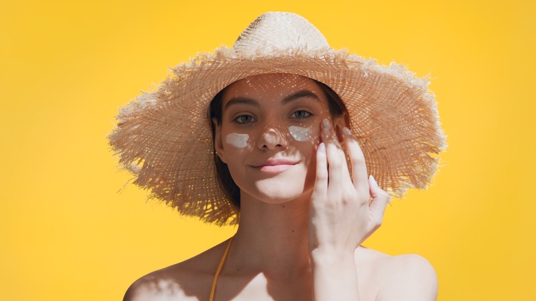 Woman with a sun hat applying sunscreen to her face