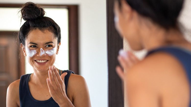 woman moisturizing face in mirror