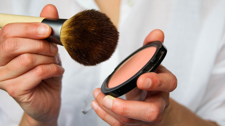 woman tapping blush onto brush