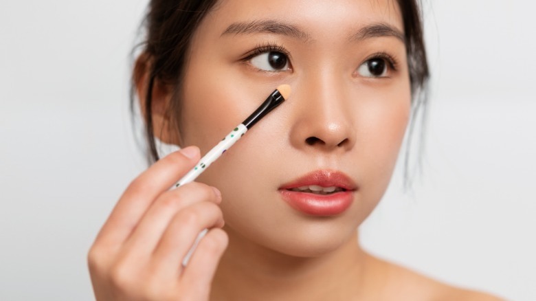 Asian woman applying concealer