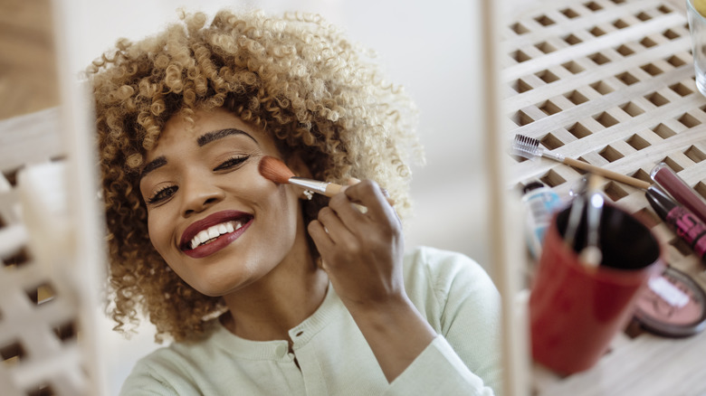 Woman applying blush to upper cheek