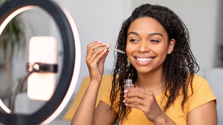 smiling woman applying serum using dropper with ring light