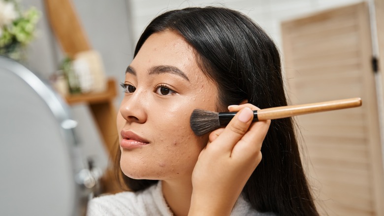 Woman applying makeup to blemishes