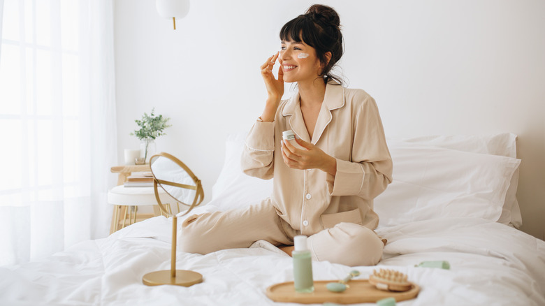 Person applying face cream in bed