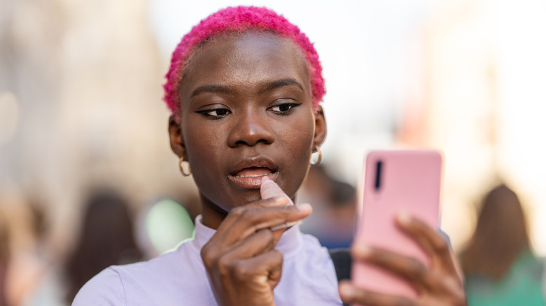 Woman applying lip gloss with phone