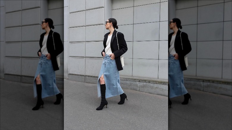 woman with hands in her pockets wearing blue midi denim skirt, white shirt, and black blazer