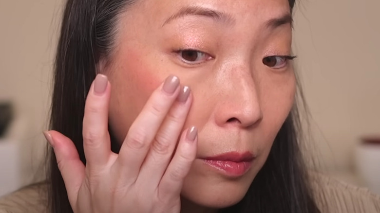 woman applying cream blush to cheek