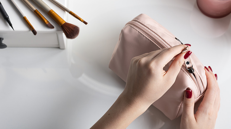 Woman unzips makeup bag on white counter