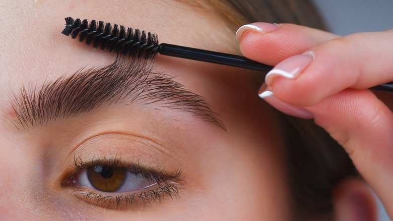 woman brushing eyebrow with spoolie