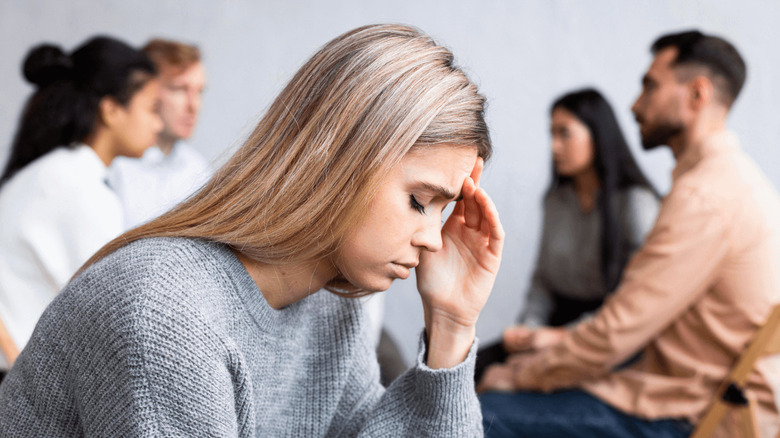 Woman feeling anxious and sitting away from group of people 