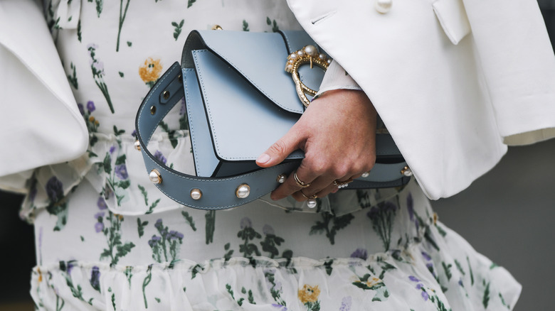 Individual carrying blue handbag with pearl embellishments