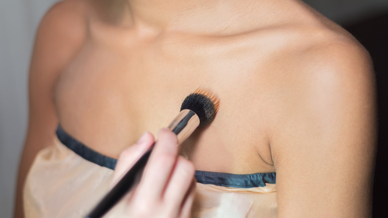 Applying bronzer to woman's décolletage