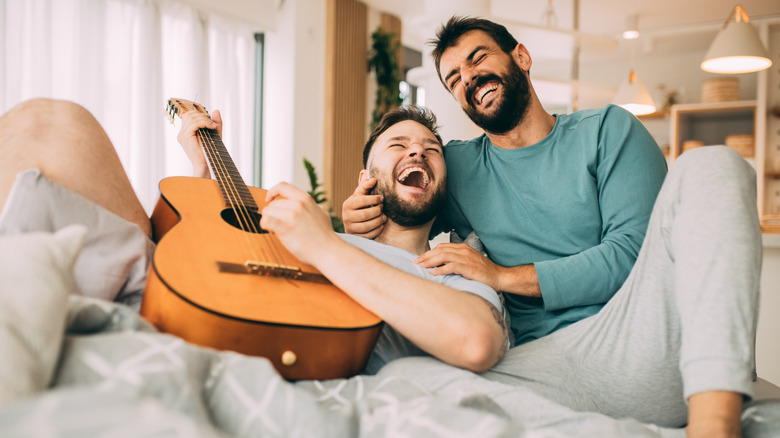 laughing gay couple cuddling with guitar
