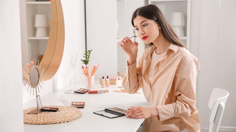 woman curling eyelashes in mirror