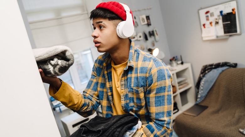young man with headphones on putting away clothes