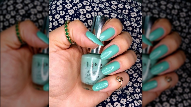 Hand holding blue-green nail polish bottle 