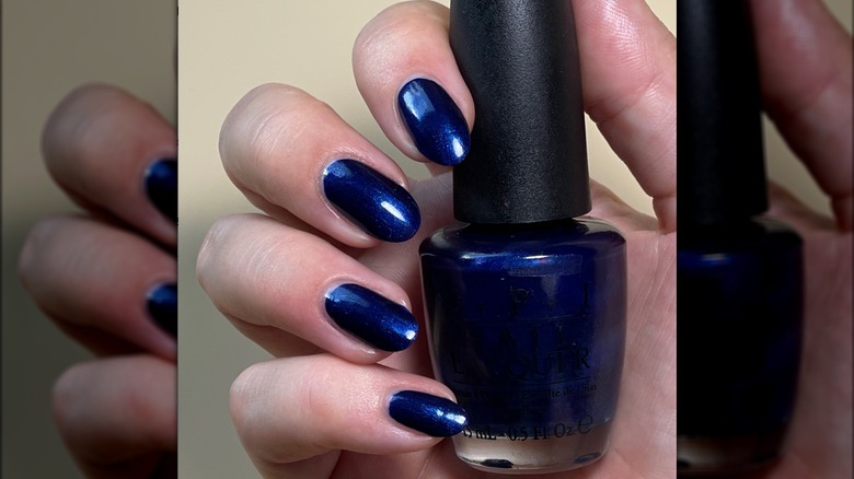 Blue fingernails holding a bottle of nail polish