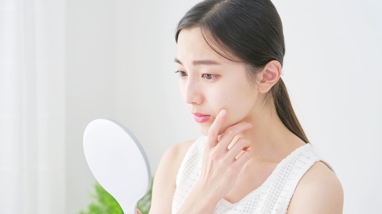 woman looking at skin in mirror 