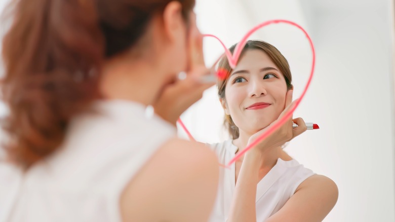 Woman looking into mirror with heart drawn on it