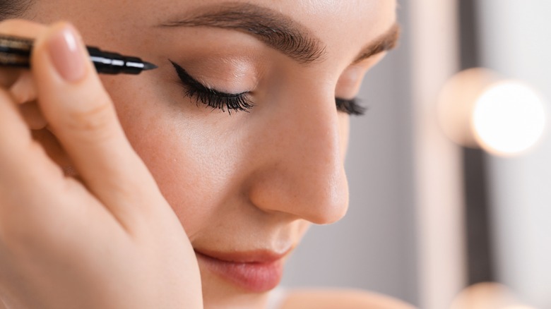 A woman applying liquid eyeliner in a small wing