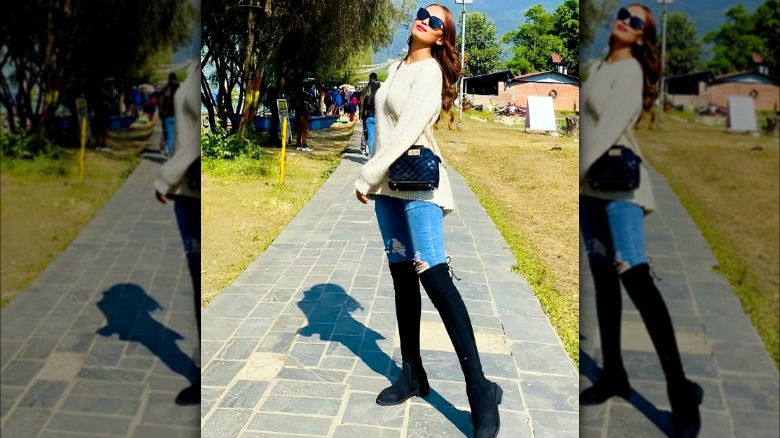 Woman poses on pathway in skinny jeans and knee-high boots