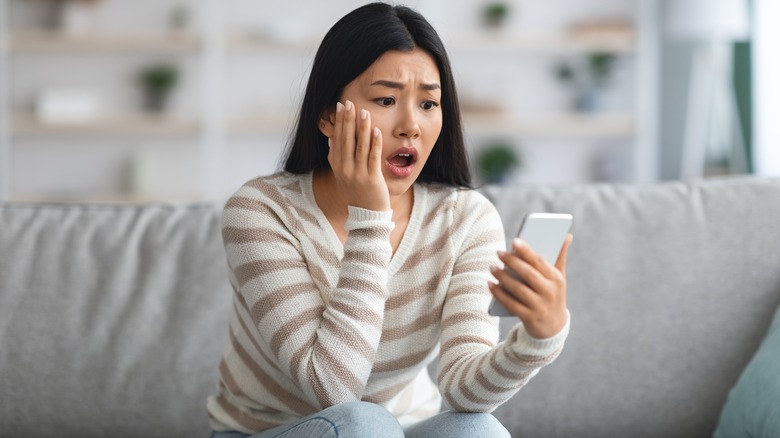 Woman looks at phone in shock